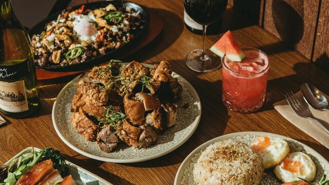 Crispy pork belly takes centre stage with its golden crackling and tender, flavourful meat. The dish A wooden dining table filled with Filipino dishes including crispy pork belly, fried rice with eggs,