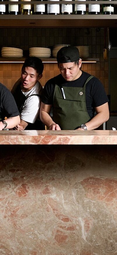 Three chefs—one particularly good looking—preparing a meal behind a bench made of Italian marble