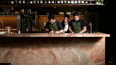 Three chefs—one particularly good looking—preparing a meal behind a bench made of Italian marble