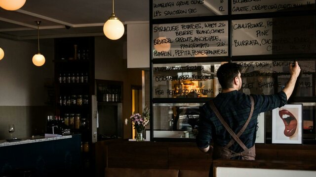 A man writes a menu on a large window glass.