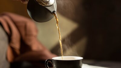 A hand pours a steaming hot tea into a cup