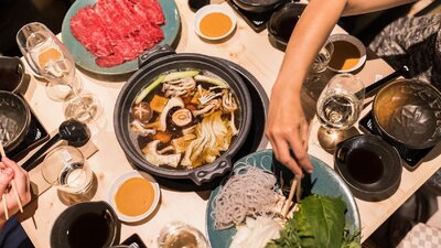 Range of Japanese dishes and hotpot with a person reaching across with chopsticks