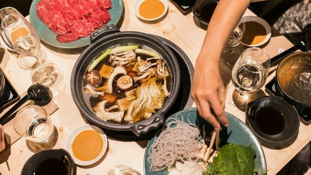 Range of Japanese dishes and hotpot with a person reaching across with chopsticks