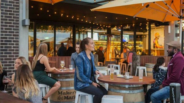 Customers seated outside at a bar with bright orange umbrellas and wooden tables.