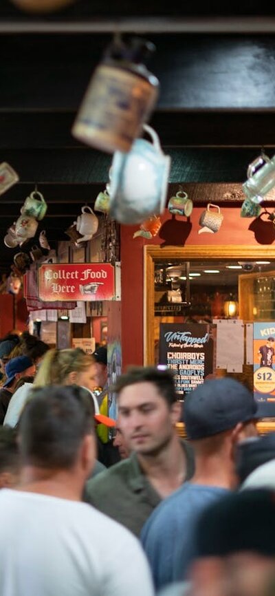 Crowd of people inside a pub, with different bottles and vessels hanging form the ceiling