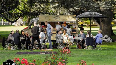 People standing and sitting on chairs and tables in front of van