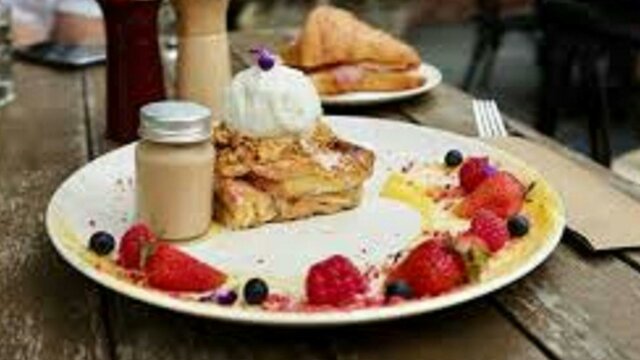 Plate lined with fruit, with pastries and jar of sauce set out on wooden table