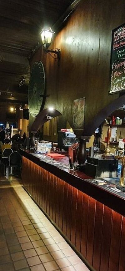 Tables and bar stools line the wall on the left, with a brightly lit bar with red tiles on the right