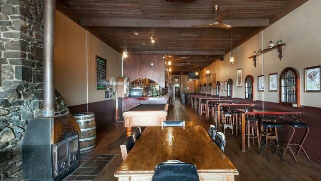 Pot belly woodfire on left-hand wall surrounded by stonework, with seating area and pool table throu