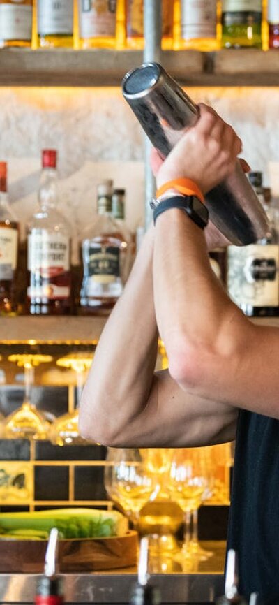 Bartender shaking up a cocktail in front of a wall of alcoholic mixers.