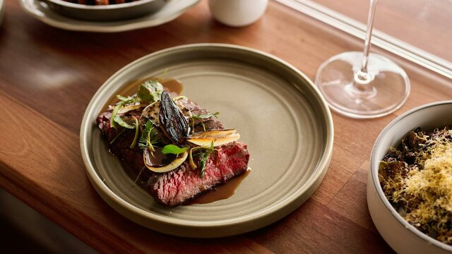 Southern Downs Wagyu Flank + Garlic Butter Wagyu flank + garlic butter, served with a glass of red wine, a side of carrots, and sprouts
