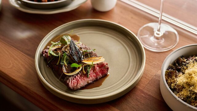 Southern Downs Wagyu Flank + Garlic Butter Wagyu flank + garlic butter, served with a glass of red wine, a side of carrots, and sprouts