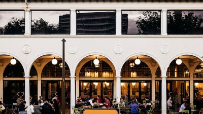 People sitting outside the building at bar tables in colonnade