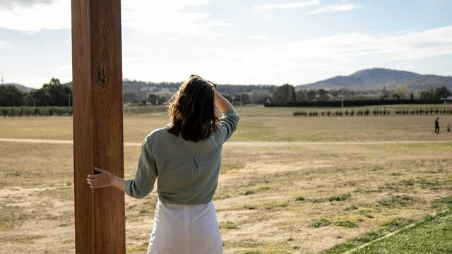 A tourist stands at a lookout, viewing vast open bush-covered fields stretching into the distance