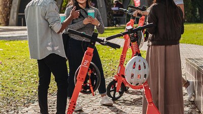 Group of people standing next to scooters on their phone