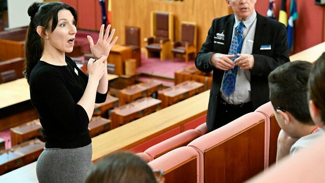 Parliament House tour guide explains the Senate chamber to visitors while an Auslan guide interprets