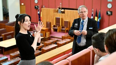 Parliament House tour guide explains the Senate chamber to visitors while an Auslan guide interprets