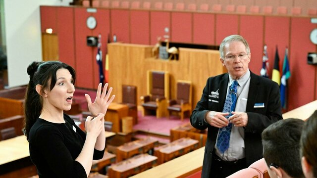 Parliament House tour guide explains the Senate chamber to visitors while an Auslan guide interprets