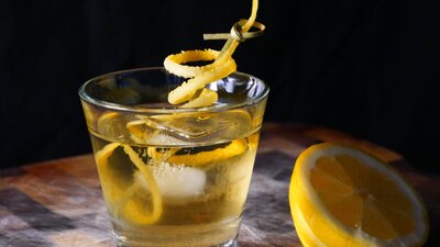 Yellow Cocktail with ice and a lemon twist.