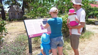 Woman holding device infront of sign with man and two children