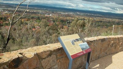 Sign leaning against stone wall with view of trees and distant houses