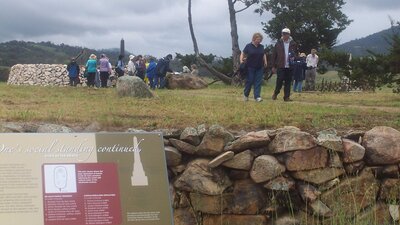 People walking on raised ground with stone wall and sign