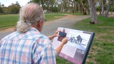 Back of man obstructing woman who has smartphone in front of sign
