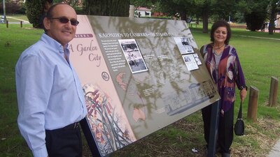 Man and woman standing at either side of sign outdoors in park.