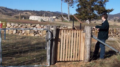 Woman standing at wooden gate looking to background with raised ground and rock walls