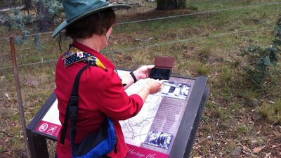 Woman in red shirt holding smart phone over an information panel in bush