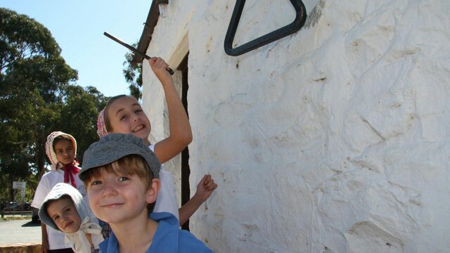 Visit the old St John's Schoolhouse at Reid Four children in 18th century dress next to a white washed wall