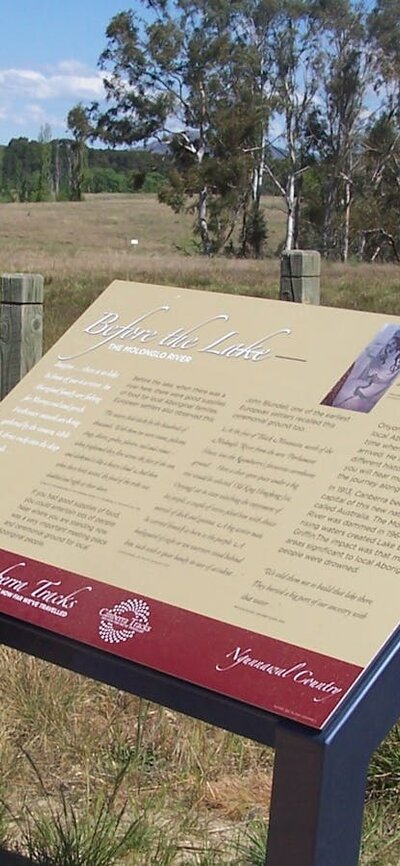Information board in grassed area with fence and water in background