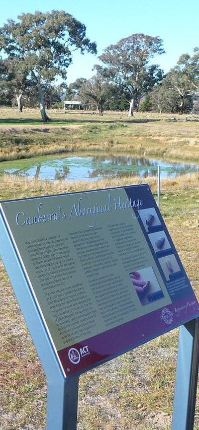 Man reading information panels in grassy area with pond