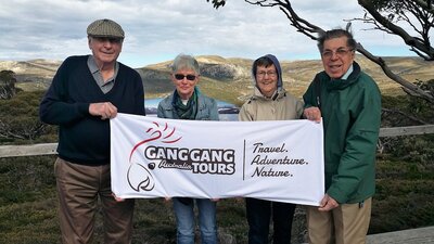 four seniors holding a gang gang tours banner with mountains behind