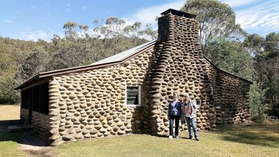 two women standing in front of hut made from river rock