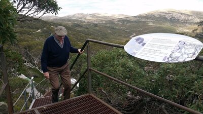 man walking up metal stairs with valley and mountains behind