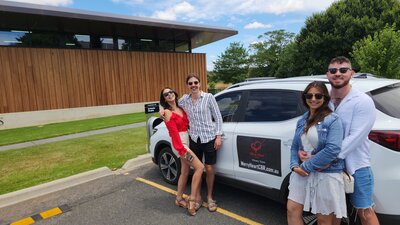 two couples embrace next to an EV car on a winery tour