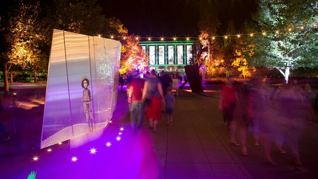 Walking past ‘Separation’, Reconciliation Place, Canberra People walk past sculpture bathed in purple light. National Library of Australia in the background