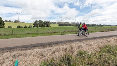 Two cyclists passing 5 wind turbines.