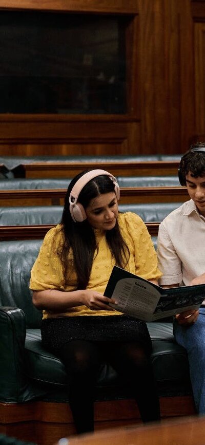 Two people seated in the House of Representatives listening to an audio guide