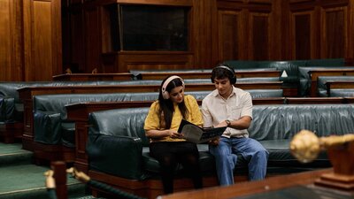 Two people seated in the House of Representatives listening to an audio guide