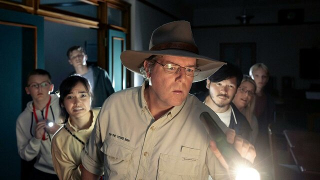 Tim holds a torch and leads a group of people through the dark halls of Old Parliament House