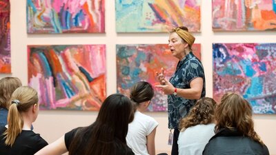 Photograph of speaker gesturing at colourful artwork in front of group