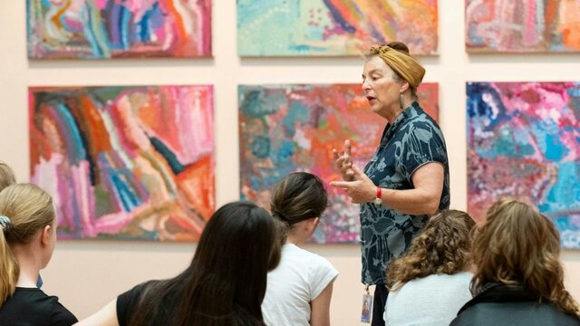 Learn School group visit Emily Kam Kngwarrey Photograph of speaker gesturing at colourful artwork in front of group