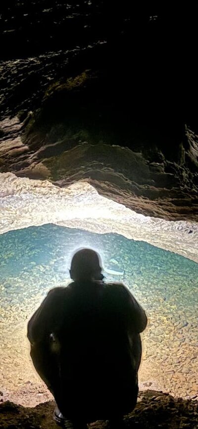 A person looking into a water filled siphon in a cave.