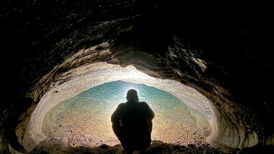A person looking into a water filled siphon in a cave.