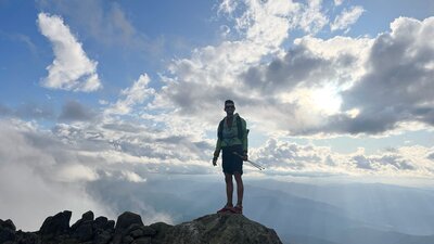 A hiker standing on a rock in the mountains with some clouds behind them.