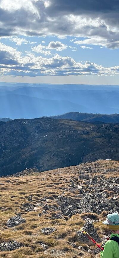 A hiker looking out into the mountains with the sun shining through the clouds.