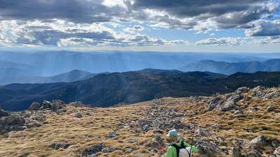 A hiker looking out into the mountains with the sun shining through the clouds.