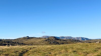 A wide open rolling mountain with bigger mountains in the distance.